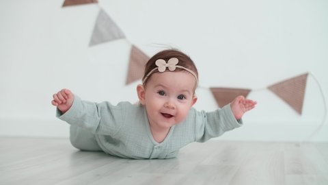 Happy Kid, Baby Care, Stay at Home, Comfort and Joy. Six month old baby girl rejoices lying on the floor and waving her hands