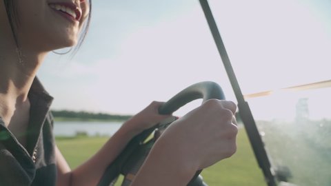 close up shot of young asian female golfer smile and happy while driving golf car inside beautiful green golf course, having fun relax on holidays summer vacation, spring valley, hot sunny weather