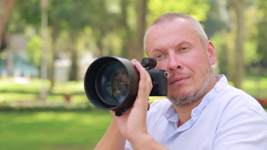 Video, an adult man makes a photo on a camera with a large lens. In the park on a sunny day in summer. | Shutterstock HD Video #1062504364