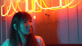 Portrait of a young beautiful Asian woman against the background of neon lights. Fast food restaurant with Asian cuisine. Large red sign with neon hieroglyphs.