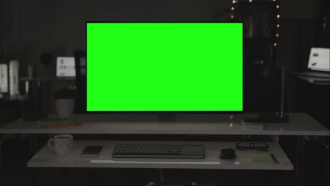 Green screen desktop computer on dark room. Several devices in the background.  Chroma key. Remote working. Home office. Put your own images or videos. Track corners with perspective corner pin.