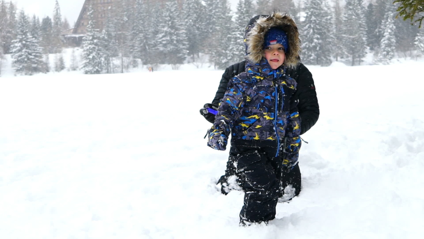 Little boy playing with his father in the snow and making funny faces in front of camera, slow motion