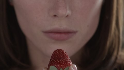 Close-up of young positive beautiful woman eating ripe delicious red strawberry