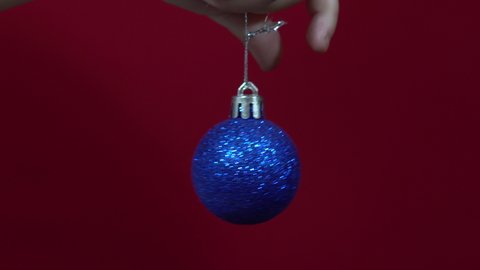 Blue christmas toy in hand on a red background close up