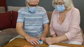 Senior couple grandparents measuring, monitoring oxygen saturation with digital pulse oximeter at home. Elderly woman and man in medical masks. Coronavirus, Covid-19 quarantine lockdown. 6k downscale - Powered by Shutterstock - Get 15% off with code: PIKWIZARD15