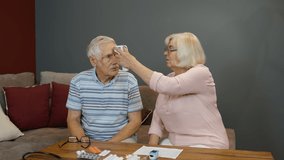 Senior couple grandfather and grandmother isolated at home during covid-19 coronavirus quarantine lockdown. Measures temperature with contactless digital thermometer. Elderly man, woman. 6k downscale - Powered by Shutterstock - Get 15% off with code: PIKWIZARD15
