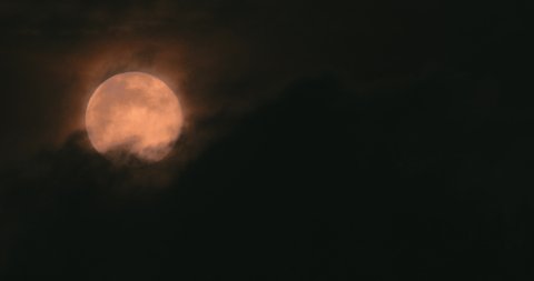 Full red moon moves through the night sky, accompanied by small clouds.