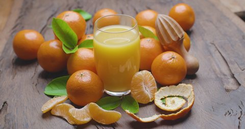 Glass of tangerine juice surrounded by ripe tangerines with leaves on an old wooden surface.