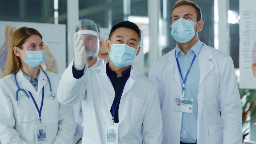 Diverse young doctors team communicating in medical office wearing masks agree to nee vaccination applauding successful meeting. Professional staff. Quarantine. Coronavirus. | Shutterstock HD Video #1062517192