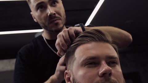 A young male Barber adjusts the hair of a male client. Professional hair care products.