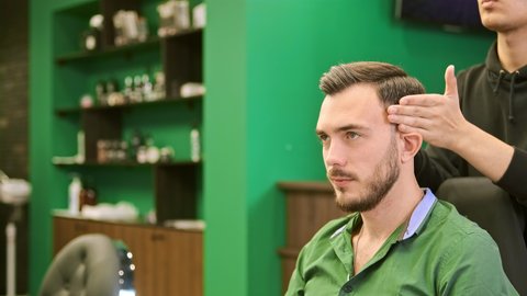Young barber styles serious client man dark hair with warm wax skillfully in professional barbershop close view slow motion