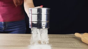 Girl pours flour from a metal mug on a wooden table in slow motion, on a dark background