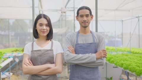 Two Asian couple farmers owner working in vegetables hydroponic farm with happiness. Man and woman crossing arm and looking at camera with smile and happiness and proud in the green house farm.