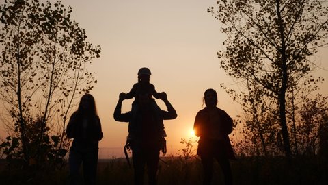 happy family tourists go hiking in the park sunset silhouette. adventure travel concept. teamwork. happy family a tourists with backpacks hikers go camping sun. teamwork group people park walking