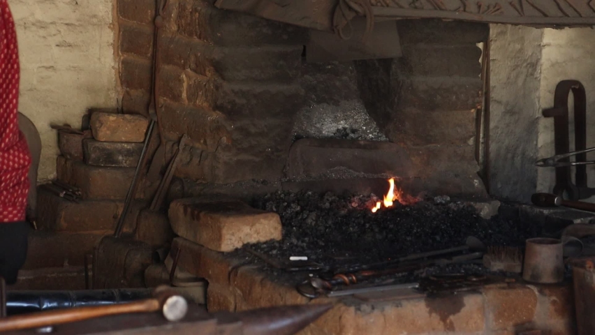 Blacksmith and apprentice removing red hot pieces of metal from an old time forge