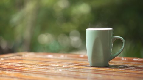 Hot coffee cup with smoke on wood table top in bokeh green nature background 