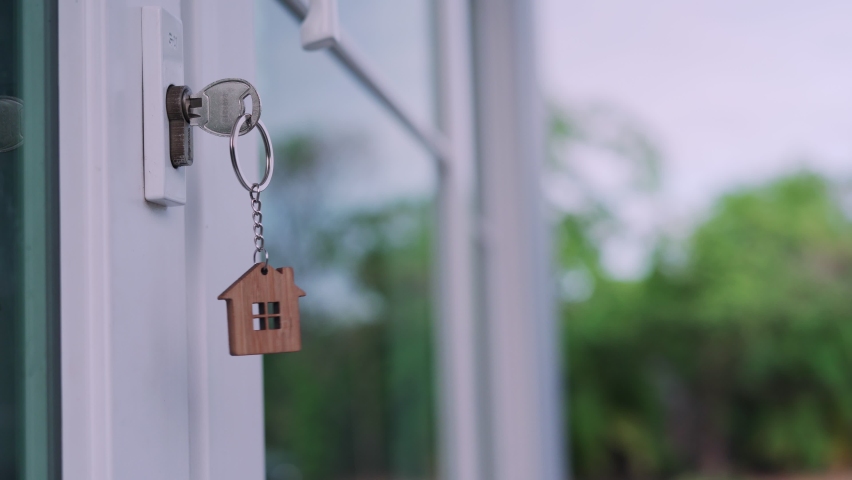 The house key for unlocking a new house is plugged into the white door. The keychain is moving after the wind blows. house for sell concept. | Shutterstock HD Video #1062528616