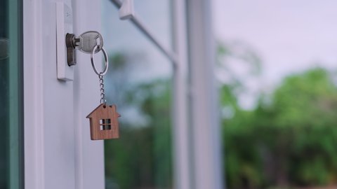 The house key for unlocking a new house is plugged into the white door. The keychain is moving after the wind blows. house for sell concept.