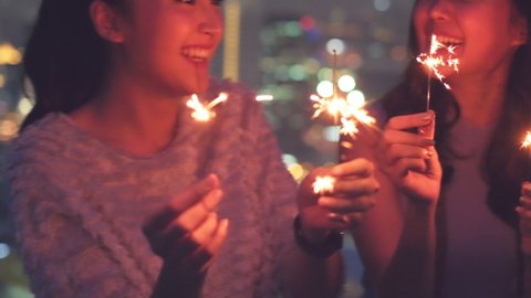 Young asian woman with sparklers is dancing and celebrating a new year. Fireworks, bengal lights in slow motion. Having fun at rooftop in the city.close up sparklers portrait.