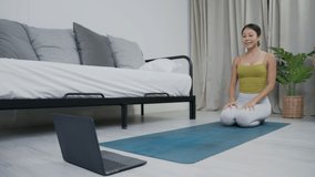 Asian woman practicing yoga online on laptop at home. meditating alone on the floor with eyes closed, Yoga, balance, meditation, relaxation, healthy lifestyle, self-care, online training class concept