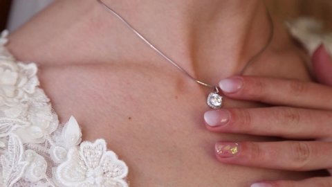 Girl in white dress with golden chain around her neck. bride fixes a decoration of jewely with well-groomed hands on the neck . wedding details. pendant details for women's neck