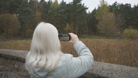 Shooting video on a smartphone of the autumn landscape. Elderly woman shoots video on smartphone