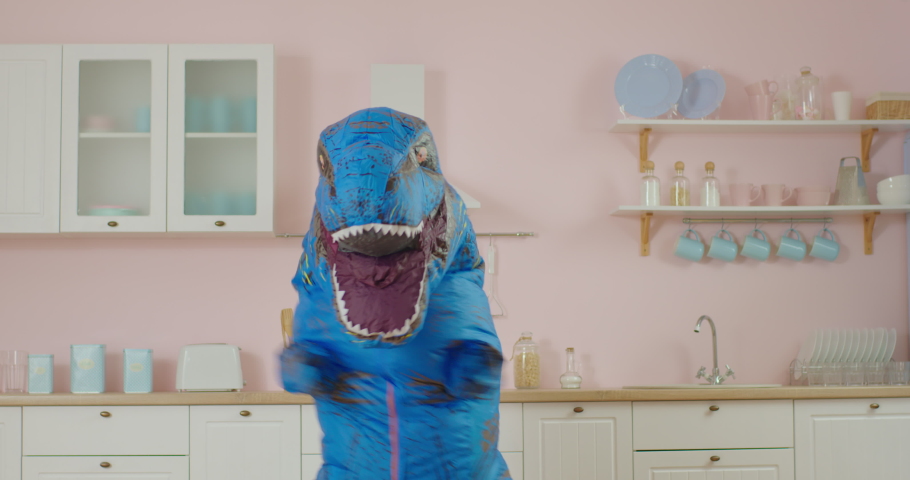 Funny dancing of blue dinosaur at pink kitchen. Comical movements of person in dino mascot. Slow motion fun dance. | Shutterstock HD Video #1062545686