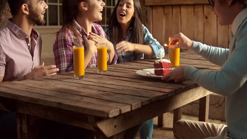 4k wide video of young budget conscious, multicultural group of friends celebrating a birthday with slice of cake and candles at a cafe. 