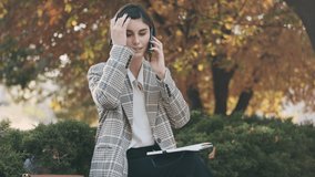 Young attractive businesswoman talking on smartphone and making notes in her diary on street. Stylish lady working outdoor