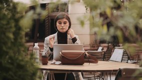 Young beautiful businesswoman looking in laptop and preening before video call with customers during coffee break in cafe outdoor 
