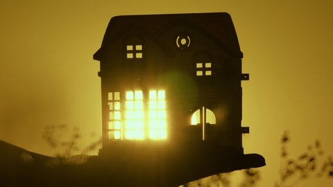 Hand silhouette with a toy house in rays of warm sun, rays of flash through windows and doors. in palms of the child dream of his home. family beautiful home concept. beautiful real estate at sunrise.