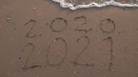 Message Year 2020 replaced by 2021 written on beach sand background. Good bye 2020 hello to 2021 Lapping waves happy New Year coming concept