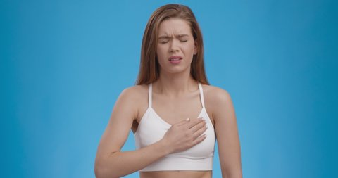 Heart attack threat. Caucasian woman feeling strong ache in chest, writhing in pain, blue studio background