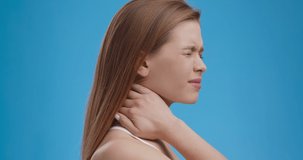Neck pain. Tired woman suffering with painful feelings in neck muscles, blue studio background, side view. Health care and medical concept