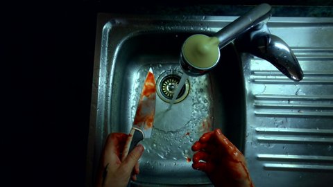 Top view cinematic scary shot of scared panicking man try to wash blood off hands and knife in metal sink. POV of killer or butcher get rid of evidence and incriminating clues on crime scene