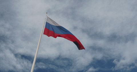 National flag of Russia waving in the wind against blue sky with clouds. Russian flag on sky background.