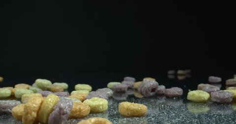 Spilled Colorful Cereal Hoops on the glossy surface. Close up shot of healthy multicolored cereal. Zoom out..