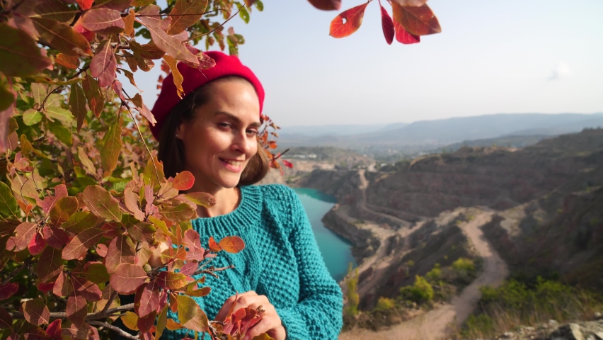 Young beautiful sensual woman in a red sweater and beret posing against the backdrop of an azure lake in the shape of a heart and autumn red foliage. Fashionable video portrait