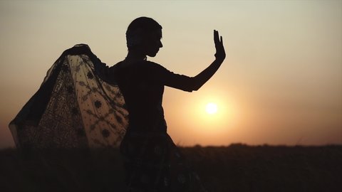 Silhouette of beautiful lady wearing gorgeous traditional dress performing bollywood festival show. An elegant Indian woman in ethnic sari dancing traditional oriental dance. Asian culture lifestyle.