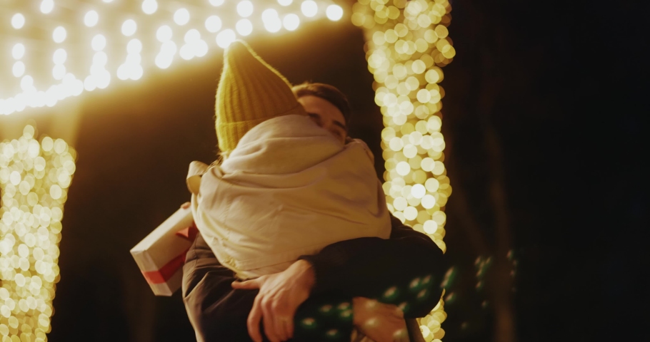 Young woman meeting up with boyfriend on birthday christmas evening party hugging tightly together swinging on the street. Illumination. Beautiful love couple. | Shutterstock HD Video #1062557854