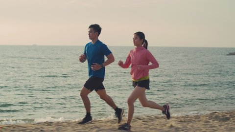 Active couple jogging outdoors during sunrise at the seaside, Asian couple running in nature living healthy lifestyle concept.
