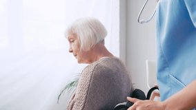 geriatric nurse moving aged woman in wheelchair