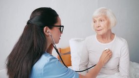 brunette nurse examining aged woman with stethoscope