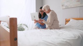 aged woman pointing with finger while using laptop together with nurse