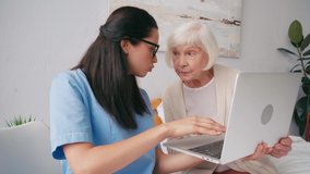 brunette geriatric nurse showing aged woman how to use laptop