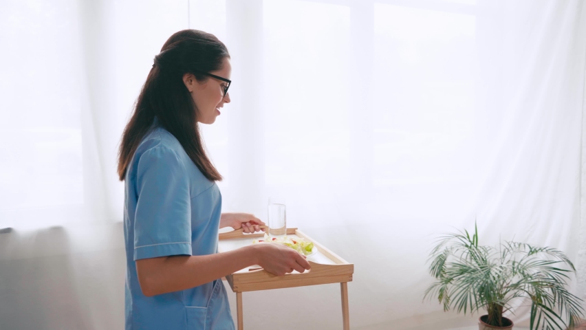 young nurse carrying tray with breakfast to aged patient Royalty-Free Stock Footage #1062564157