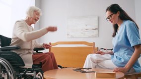 cheerful disabled woman and nurse giving high five while playing dominoes