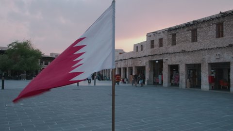 Doha, Qatar- November 18 2020: Souk Waqif Doha, Qatar main street sunset panning shot showing  Qatar flag in foreground ,  locals and visitors walking