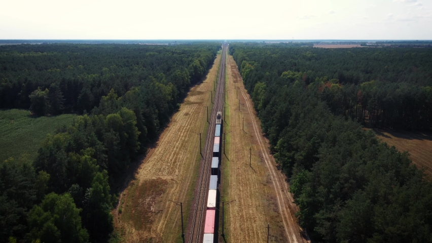 Electric locomotive with freight cars or railway wagon rides on railroad. Transportation and delivery of cargo in containers between cities and countries. Aerial view over train riding through forest Royalty-Free Stock Footage #1062564886