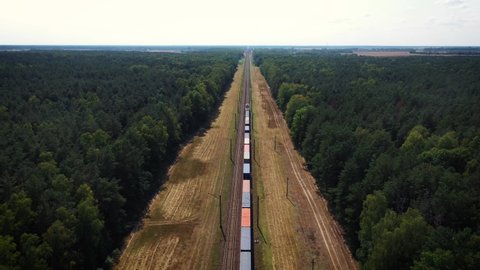 Electric locomotive with freight cars or railway wagon rides on railroad. Transportation and delivery of cargo in containers between cities and countries. Aerial view over train riding through forest